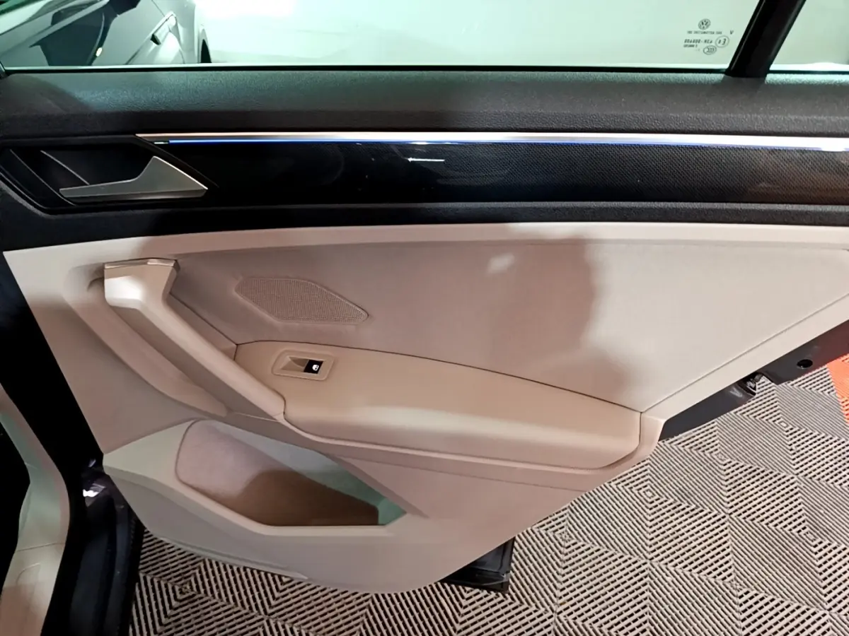 Vue intérieure côté gauche de la porte beige du Volkswagen Tiguan 2022 avec bande décorative noire et bouton de lève-vitre.