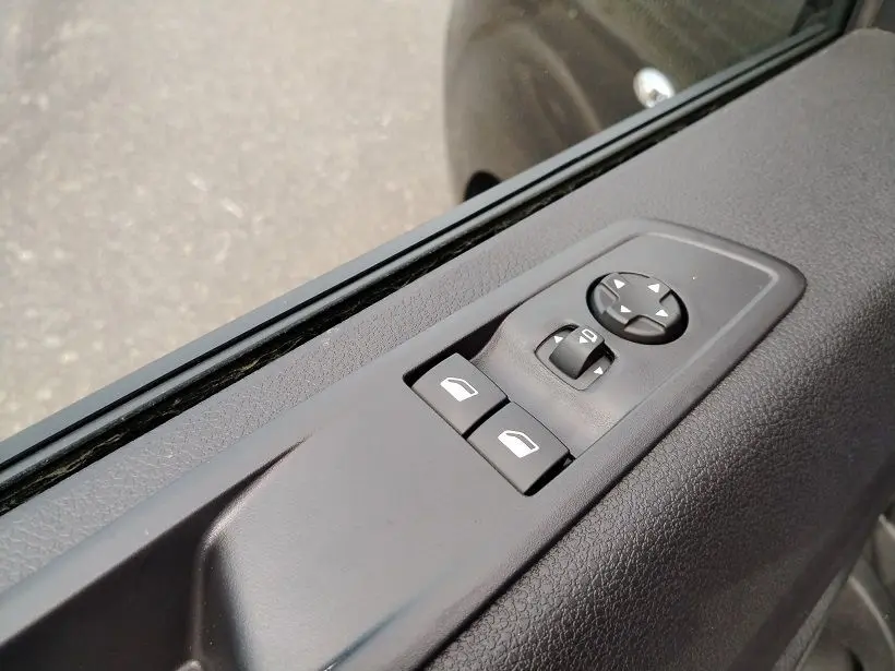 Gros plan sur les commandes de lève-vitres et rétroviseurs sur la porte côté conducteur d'un Citroën Jumpy gris titane.
