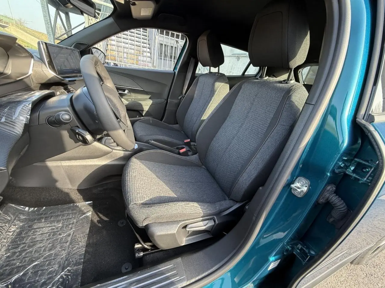 Vue intérieure côté conducteur du Peugeot 2008 2025 bleu obsession, montrant les sièges tissus gris et le volant.