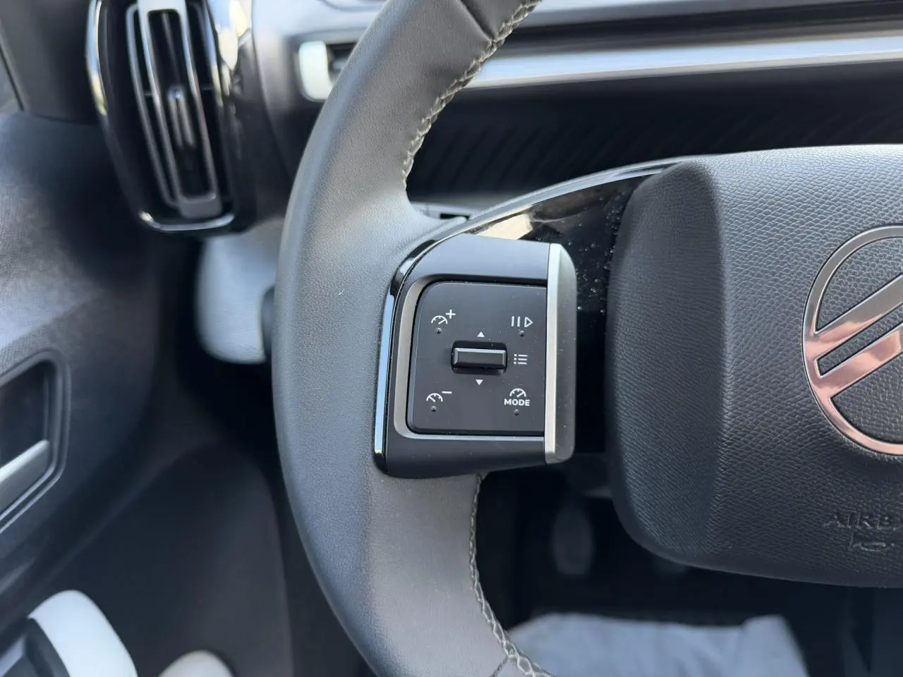Gros plan sur la commande de régulateur de vitesse à gauche du volant noir du Citroën C3 Turbo 100 Max.