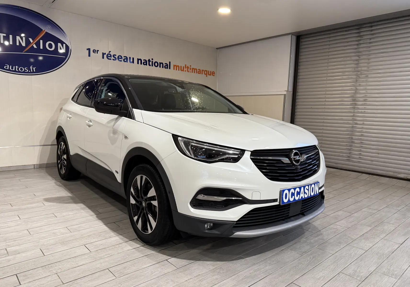 Vue 3/4 avant d'un Opel Grandland X blanc hybride rechargeable avec toit noir et jantes alliage bicolores en showroom.