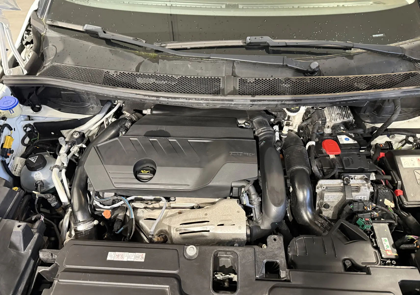 Vue rapprochée du moteur d’un Opel Grandland X blanc hybride rechargeable, avec capot ouvert et composants visibles.