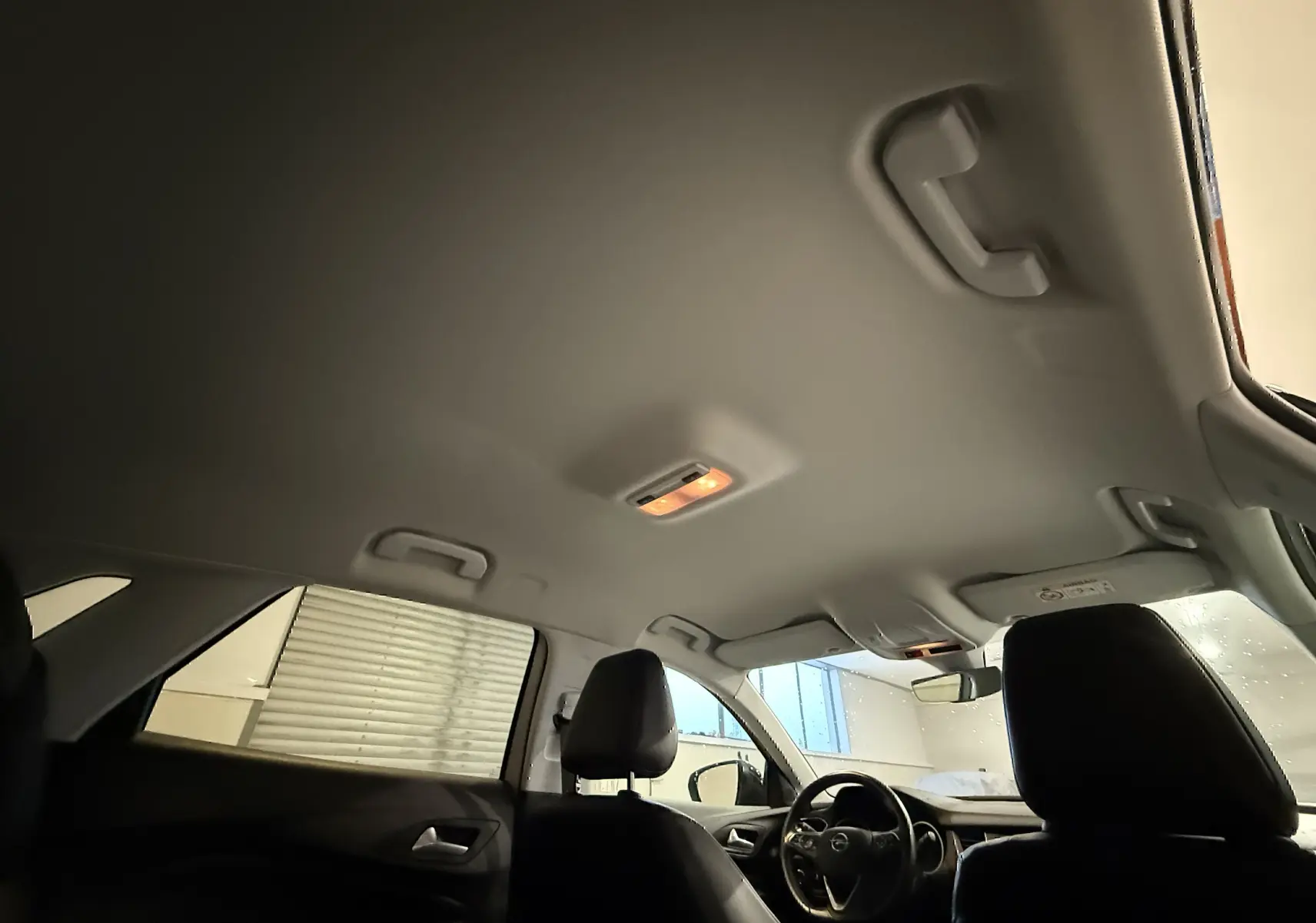Vue intérieure du plafond et des sièges avant noirs de l'Opel Grandland X blanc, avec éclairage intérieur allumé.