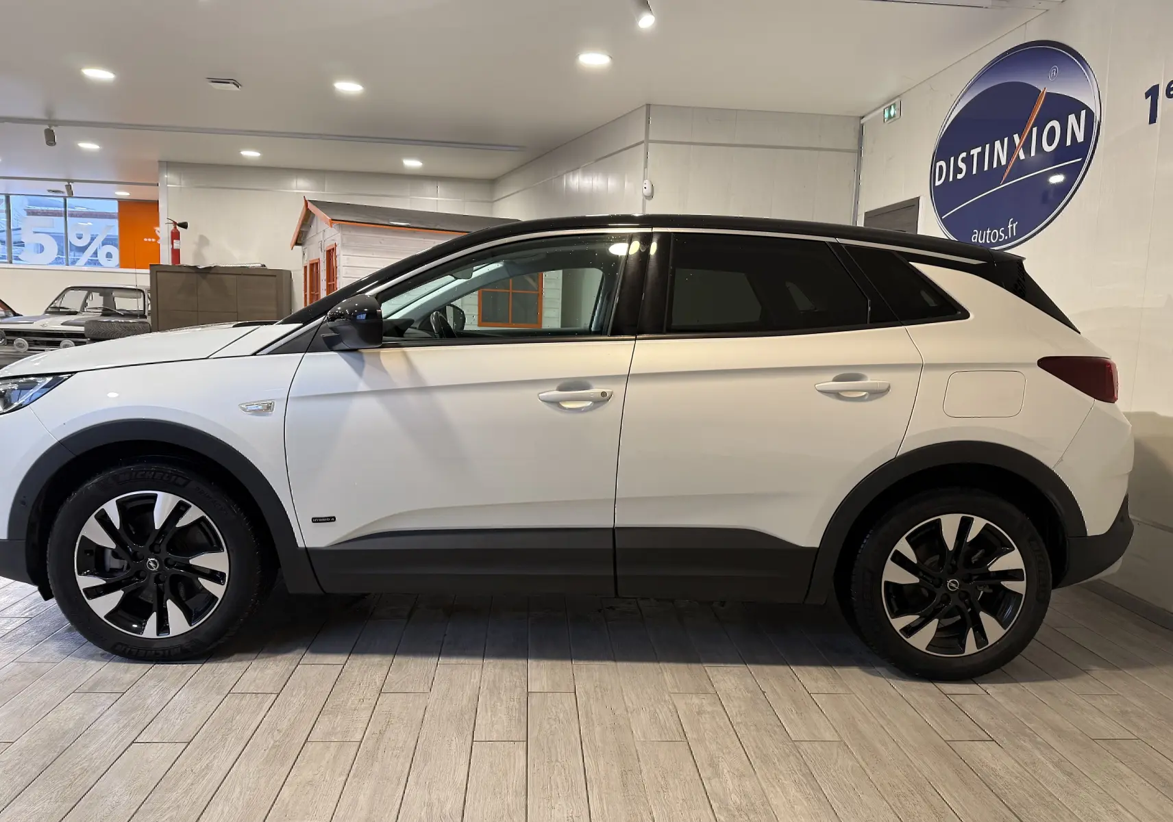 Vue de profil côté gauche d'un Opel Grandland X blanc hybride rechargeable avec toit noir et jantes bicolores en concession.