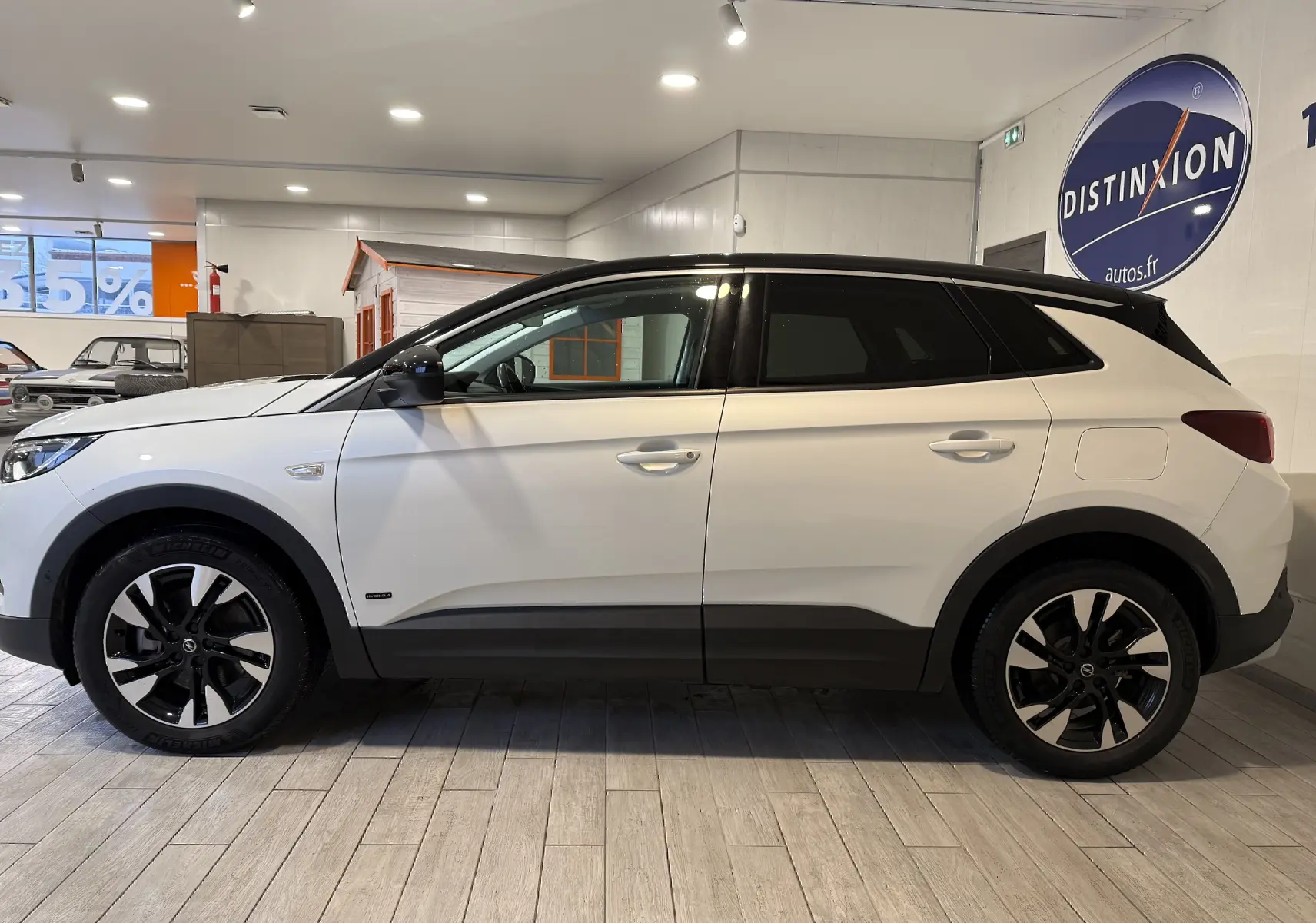 Vue de profil droit d'un Opel Grandland X blanc avec jantes noires et toit noir en intérieur showroom.