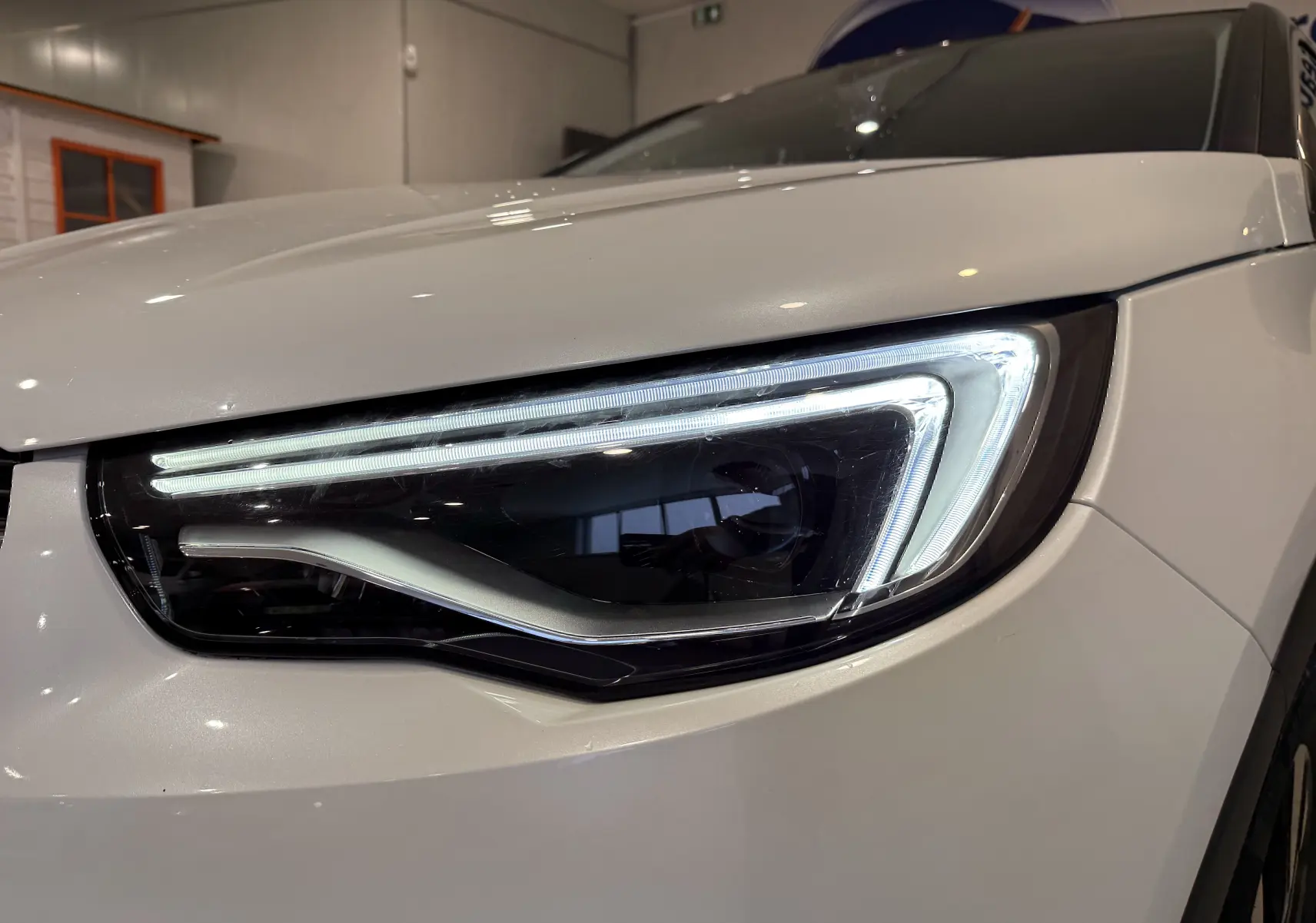 Gros plan sur le phare avant droit allumé d’un Opel Grandland X blanc, soulignant son design LED moderne.