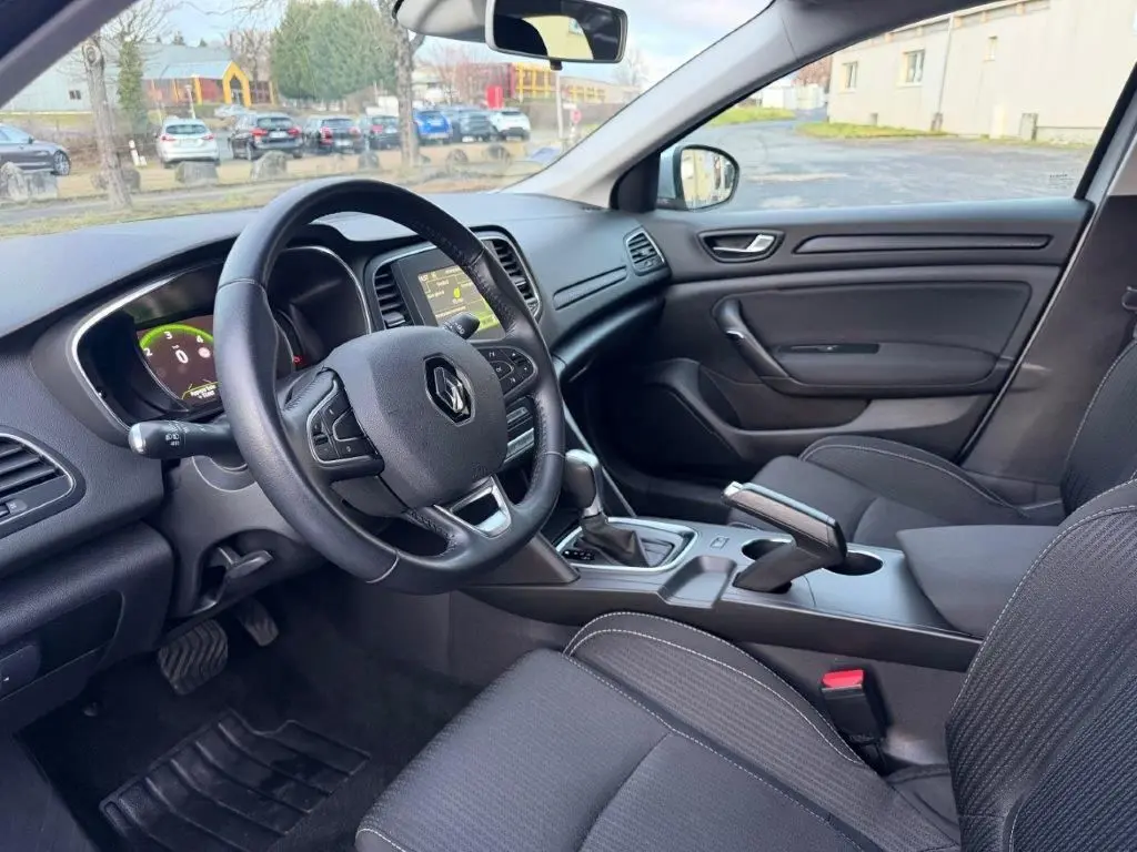 Vue intérieure côté conducteur de la Renault Mégane Business gris alu, avec tableau de bord numérique et console centrale moderne.