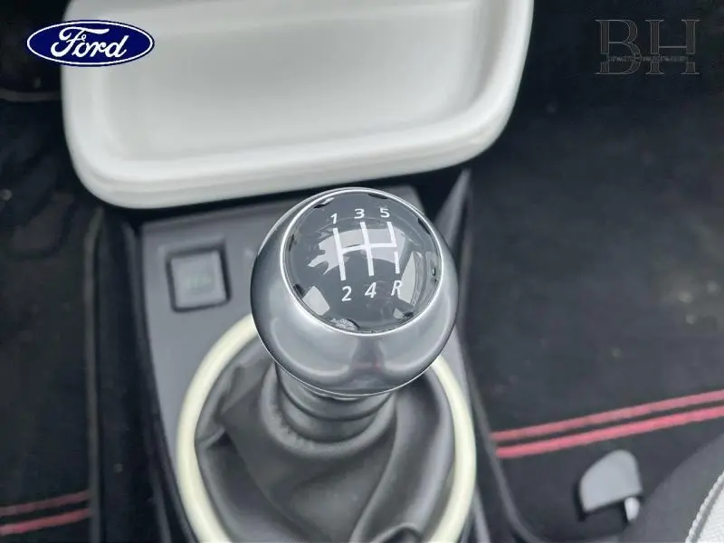 Gros plan sur le levier de vitesses manuel noir avec marquages blancs, intérieur sombre avec surpiqûres rouges visible.