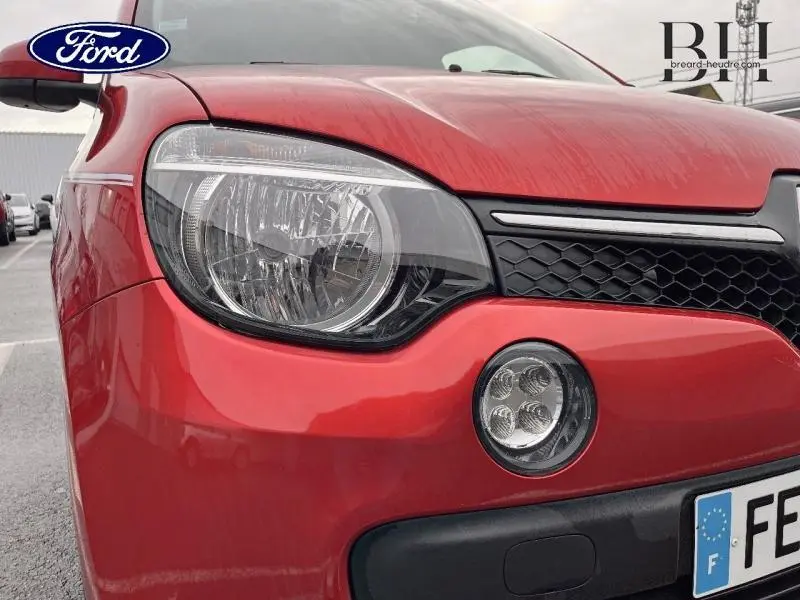 Gros plan sur l'avant gauche rouge flamme d'une Renault Twingo 2019 avec phare et antibrouillard visibles.