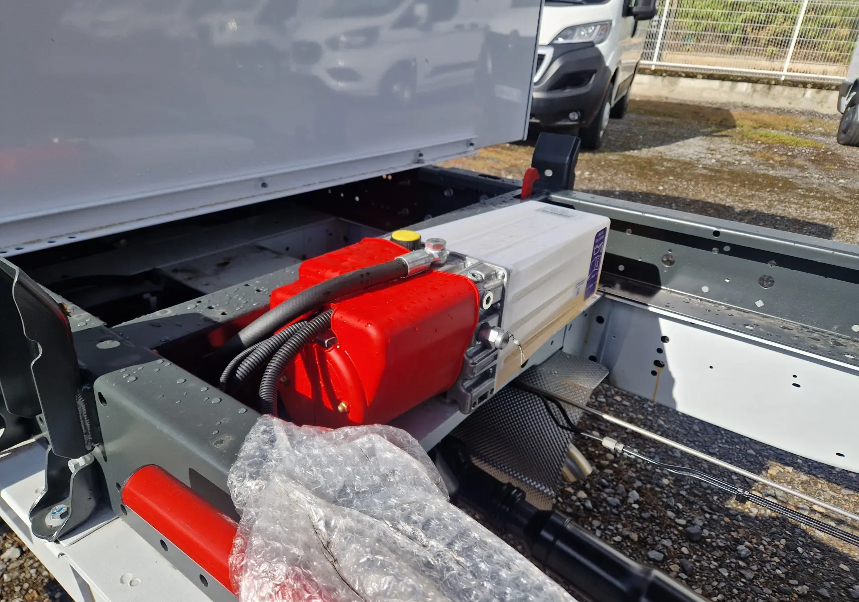 Vue rapprochée du châssis arrière du Ford Transit blanc, mettant en valeur un réservoir rouge et des câbles techniques.