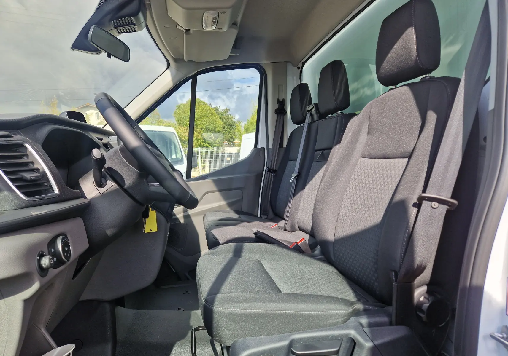 Vue intérieure côté conducteur du Ford Transit Chassis Cabine blanc, montrant les sièges tissu gris et le volant.