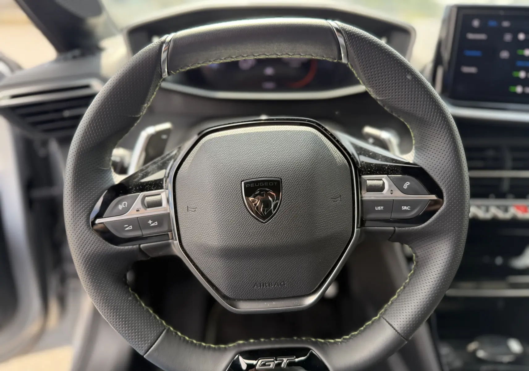Volant en cuir noir avec logo Peugeot et sigle GT au centre, intérieur moderne d'une 208 HYBRID 145 GT gris Artense.