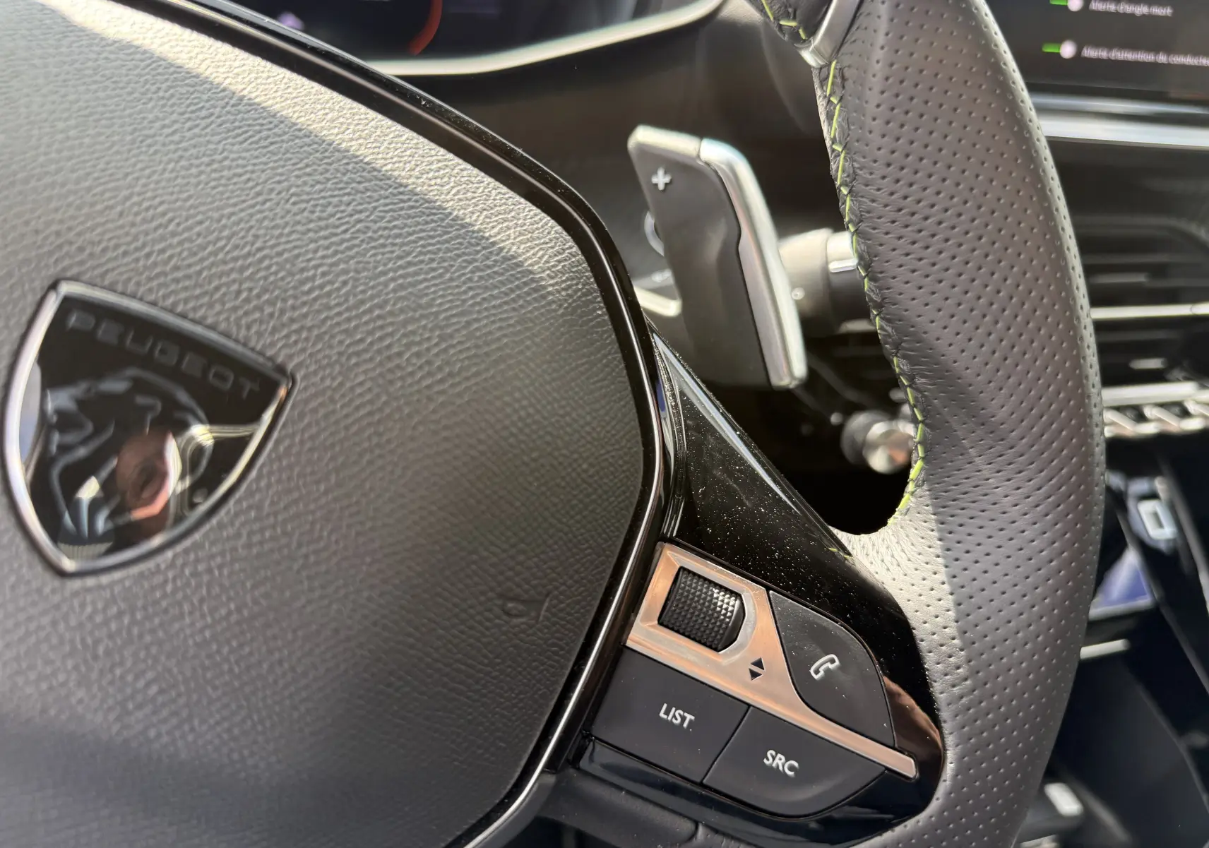 Gros plan sur le volant perforé avec surpiqûres vertes de la Peugeot 208 Hybrid 145 GT E-DCS6 de 2024.