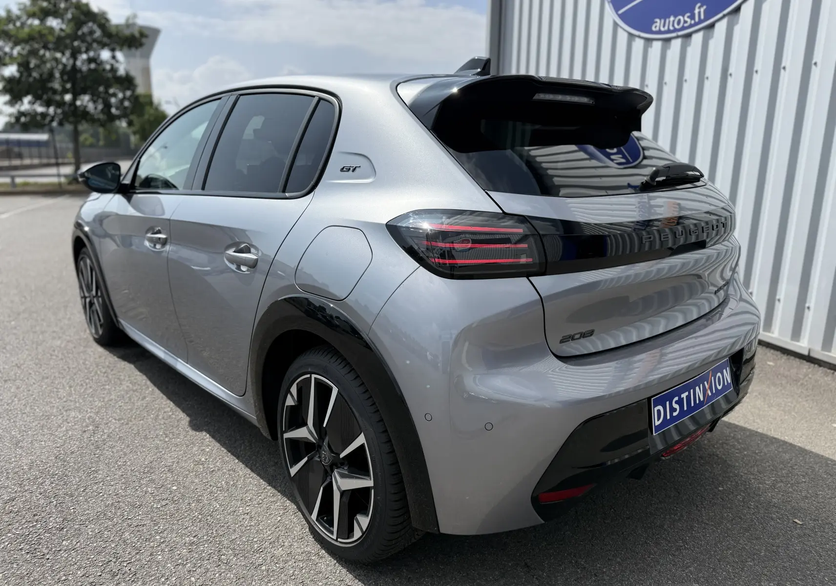 Peugeot 208 Hybrid 145 GT gris Artense vue 3/4 arrière droit avec jantes noires et logo GT sur l'aile.