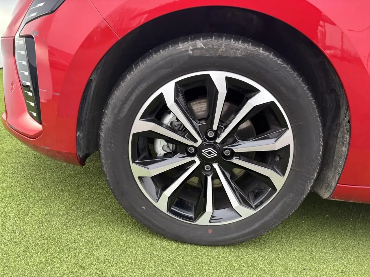 Gros plan sur la roue avant gauche de la Renault Clio V rouge flamme métal avec jante alliage noire et argent.