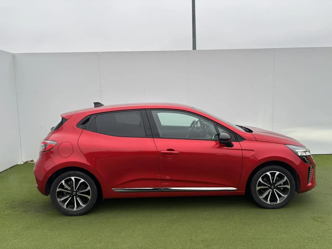 Vue de profil côté gauche d'une Renault Clio V rouge flamme métallisée avec jantes alliage et vitres surteintées.