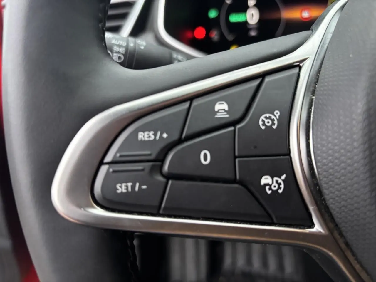 Gros plan sur les commandes au volant à gauche de la Renault Clio V rouge flamme, boutons de régulateur de vitesse et assistance.