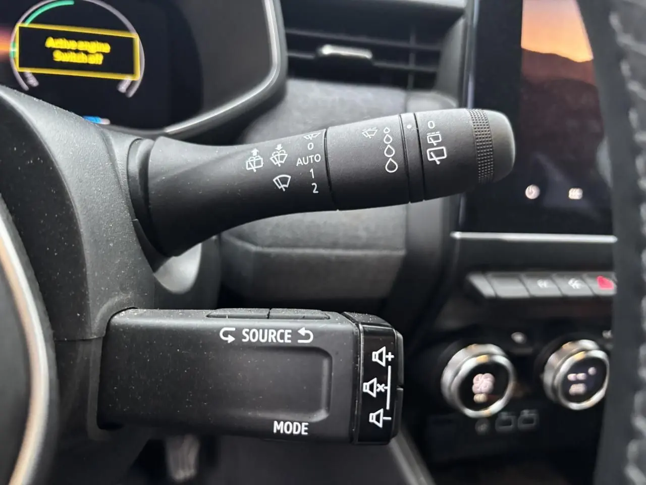 Gros plan sur les commandes au volant de la Renault Clio V hybride, avec affichage numérique partiel en arrière-plan.