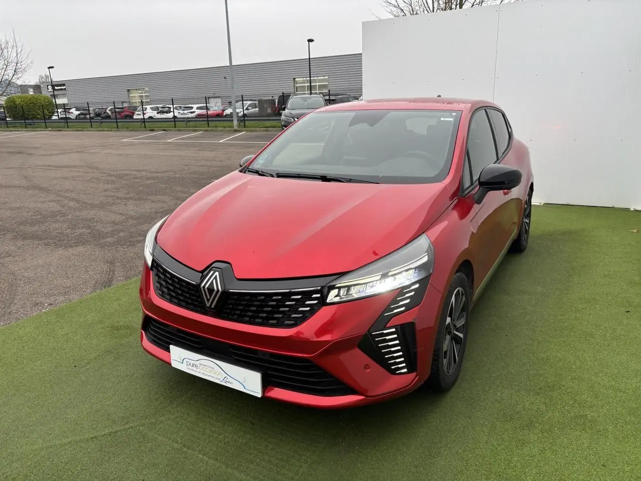 Renault Clio V hybride rouge flamme vue 3/4 avant droit, avec feux LED et calandre noire distinctive.
