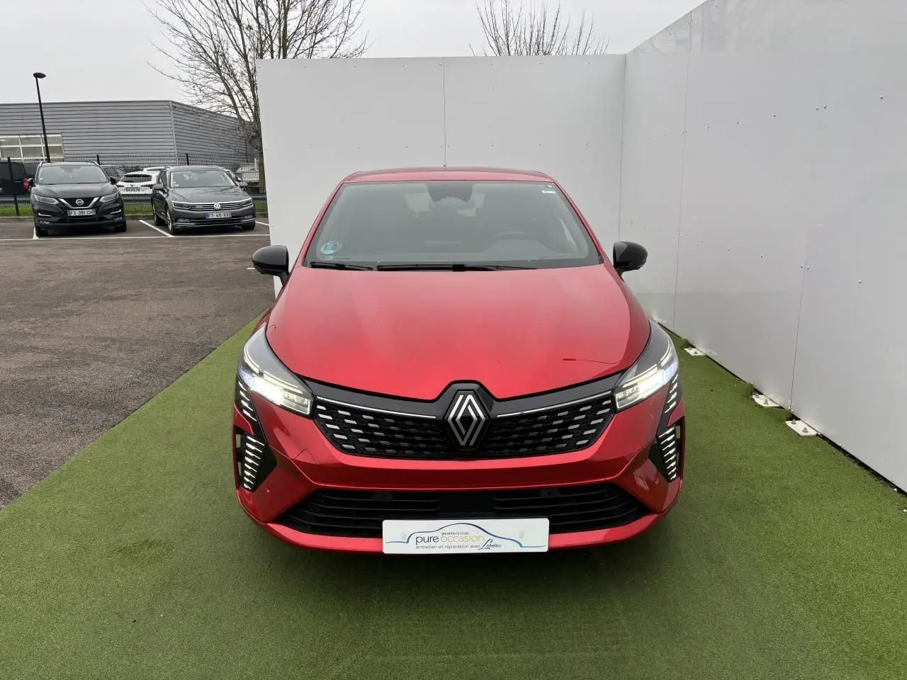 Vue avant d'une Renault Clio V rouge flamme métallisée avec calandre noire et feux LED allumés.