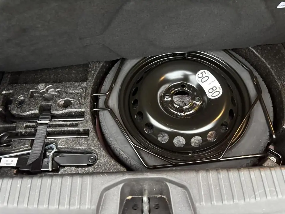 Vue rapprochée de la roue de secours noire et des outils de bord dans le coffre d'une Renault Clio rouge flamme.