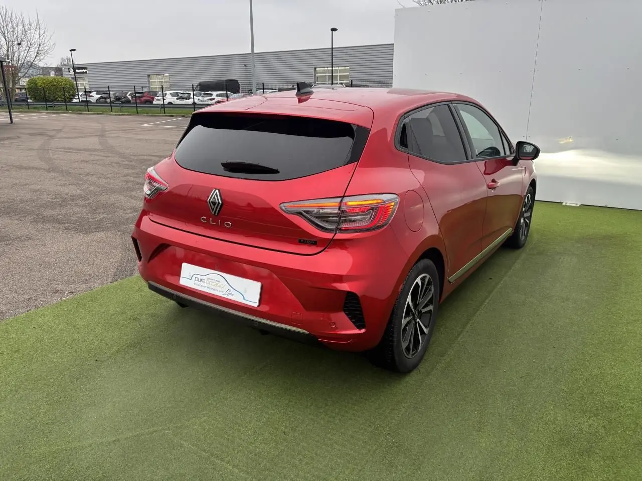 Vue 3/4 arrière droite d'une Renault Clio rouge flamme métal avec feux arrière LED et jantes alliage 16 pouces.