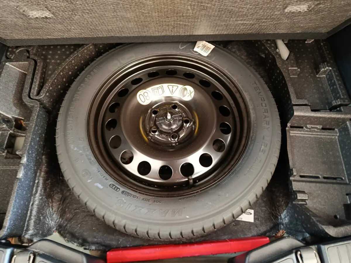 Vue rapprochée de la roue de secours noire dans le coffre du Ford Kuga 2024 bleu, avec compartiment de rangement intégré.