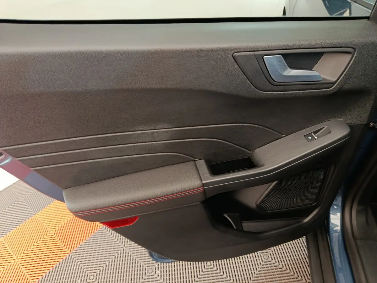 Gros plan sur la porte avant gauche intérieure noire avec surpiqûres rouges du Ford Kuga bleu 2024 St Line
