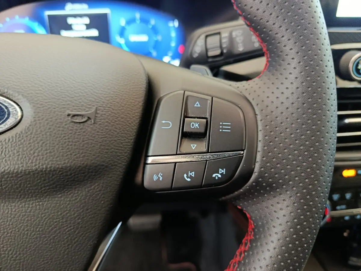 Gros plan sur les commandes du volant côté droit en cuir perforé avec surpiqûres rouges du Ford Kuga 2024 St Line.