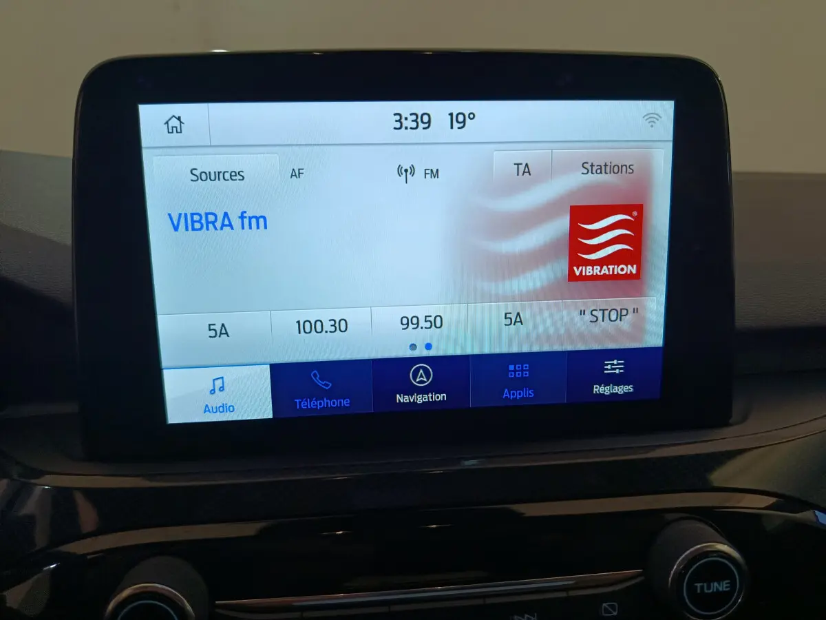 Écran tactile central du tableau de bord du Ford Kuga bleu 2024 affichant la radio VIBRA fm à 3:39 et 19°C
