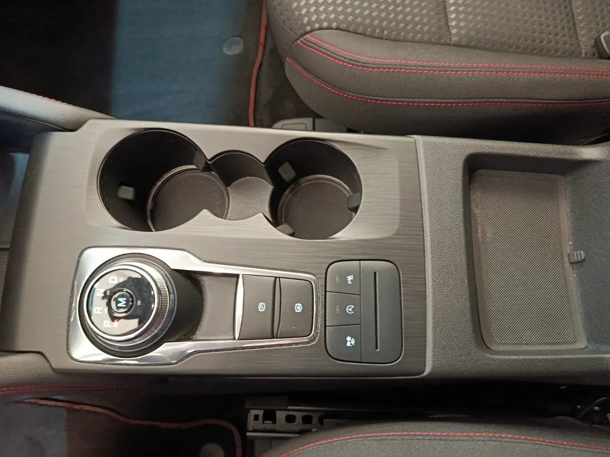 Vue plongeante sur la console centrale noire avec molette de boîte auto et surpiqûres rouges des sièges du Ford Kuga bleu 2024.