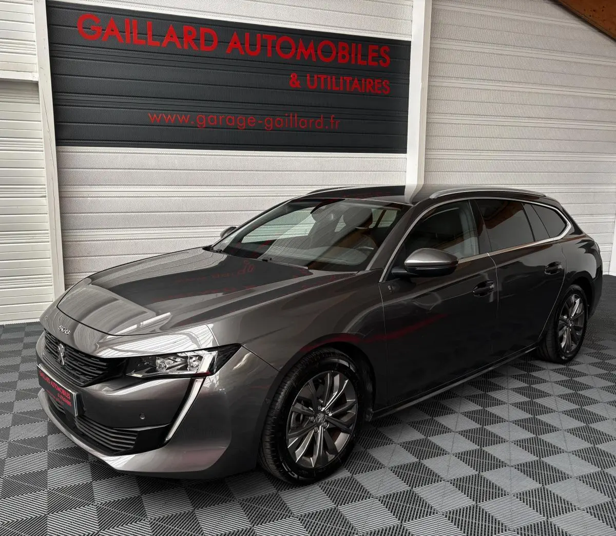 Peugeot 508 gris foncé vue 3/4 avant droit, avec jantes alliage et calandre noire brillante.