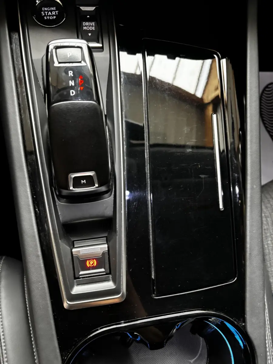 Gros plan sur la console centrale noire brillante de la Peugeot 508, avec levier de vitesse automatique et bouton frein à main électronique allumé.