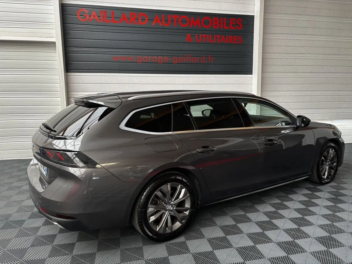 Peugeot 508 SW gris foncé vue 3/4 arrière droit dans un garage avec jantes alliage et vitres teintées.