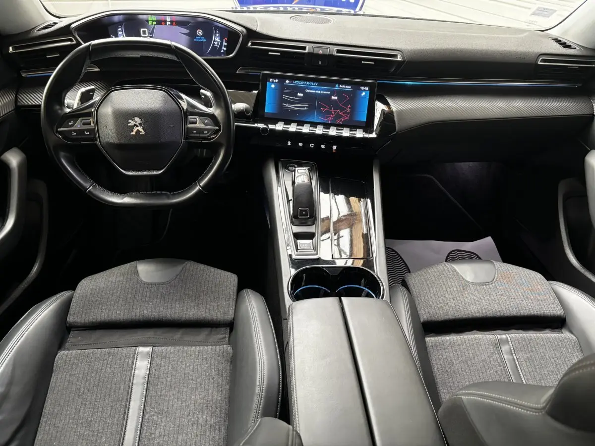 Vue intérieure avant de la Peugeot 508 gris foncé, mettant en valeur le volant cuir, l'écran tactile et la console centrale brillante.