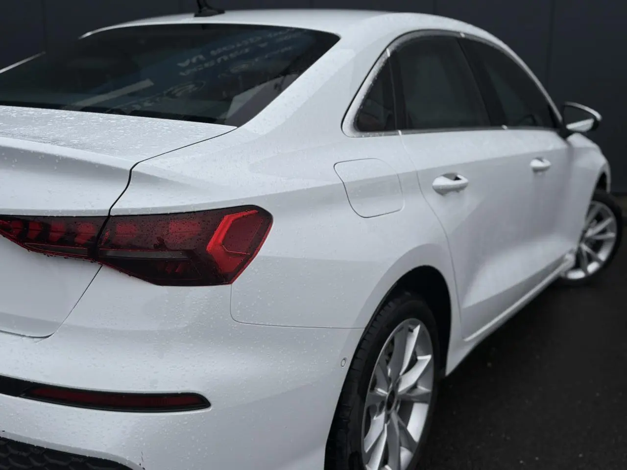 Vue 3/4 arrière droite d'une Audi A3 Berline 30 TFSI blanche Arkona avec feux arrière LED et jantes alliage 17 pouces.