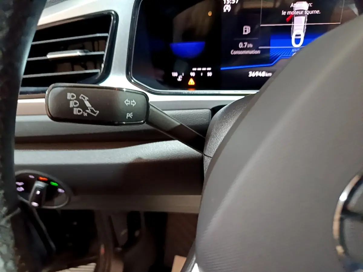Gros plan sur la manette de clignotants à gauche du volant d’un Volkswagen T-Roc gris foncé, tableau de bord numérique visible.