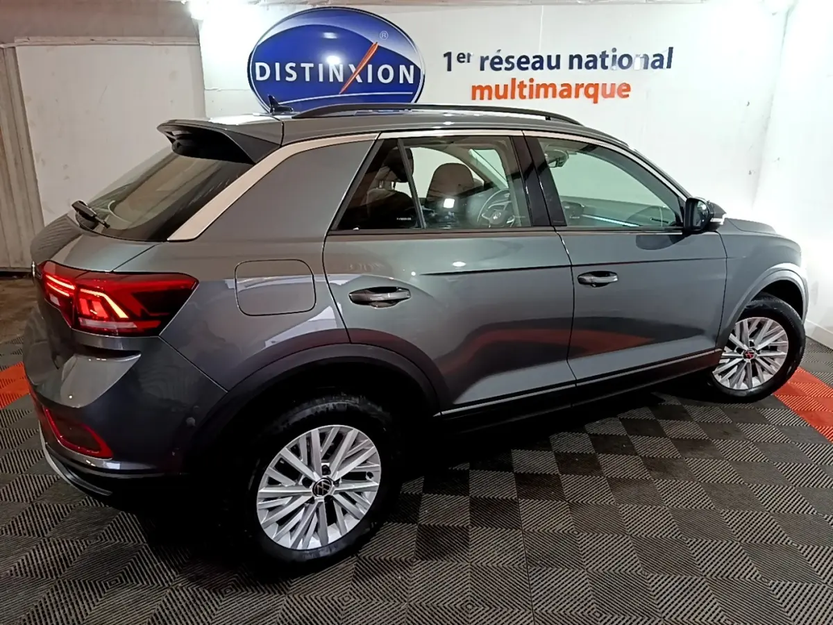 Volkswagen T-Roc gris foncé vue 3/4 arrière droit, feux arrière allumés et jantes alliage visibles.