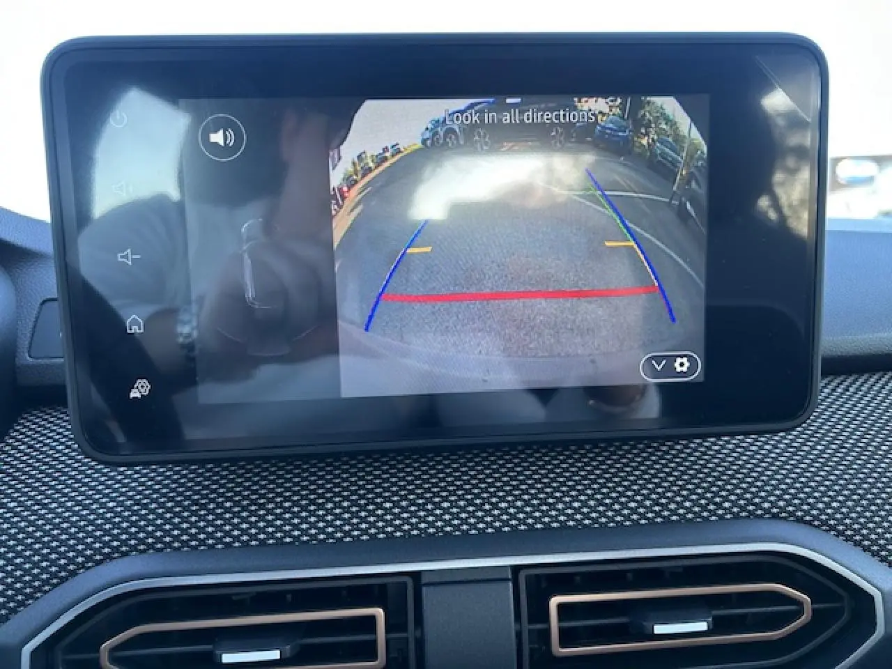 Écran tactile intérieur affichant la caméra de recul d’une Dacia Sandero Stepway blanche, avec tableau de bord texturé noir.