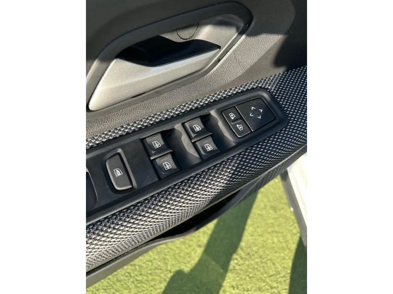 Gros plan sur les commandes des vitres électriques côté conducteur avec insert gris texturé, portière blanche visible en arrière-plan.