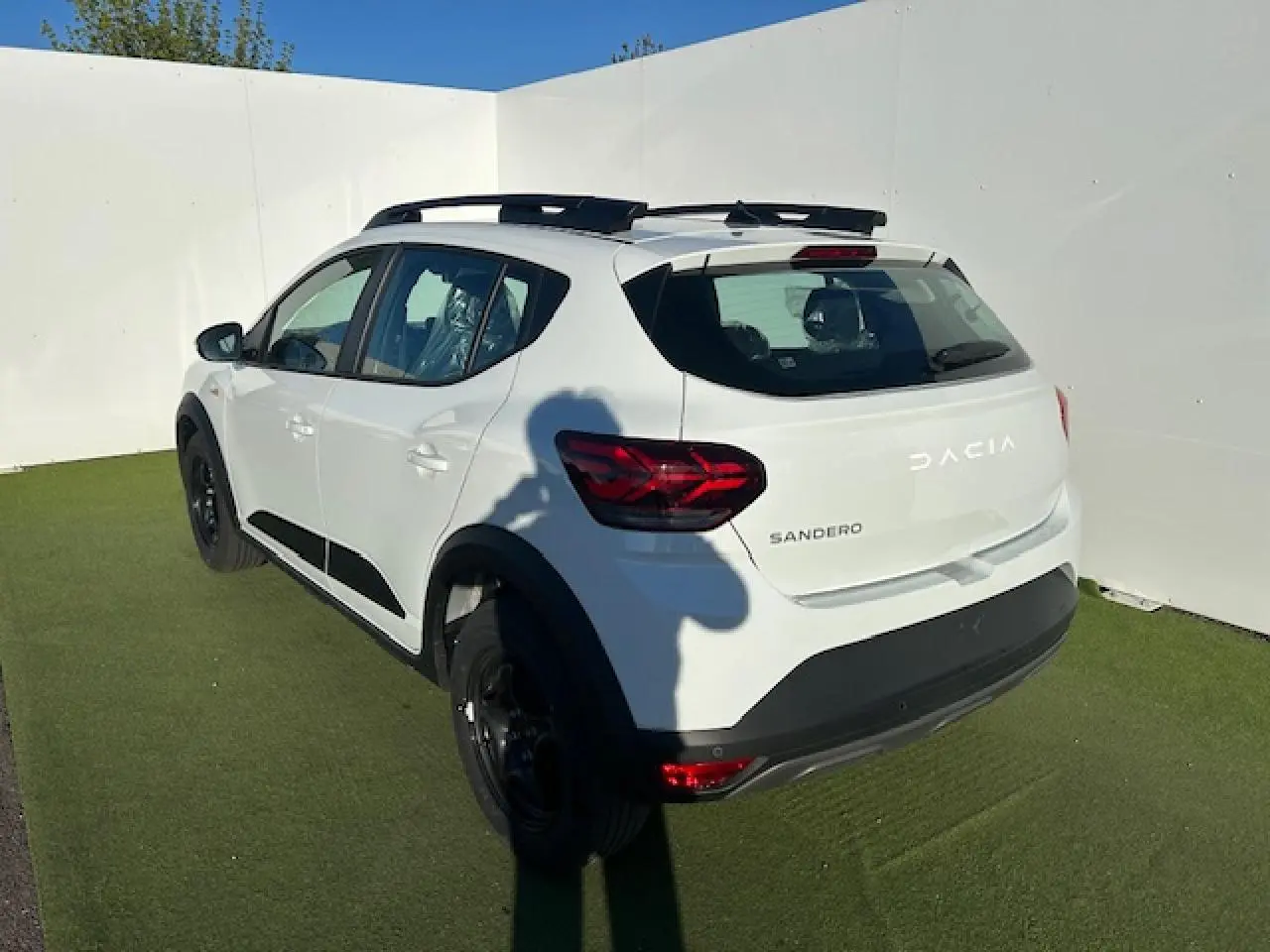 Vue 3/4 arrière droite d'une Dacia Sandero Stepway blanche avec barres de toit noires et feux arrière LED en Y.