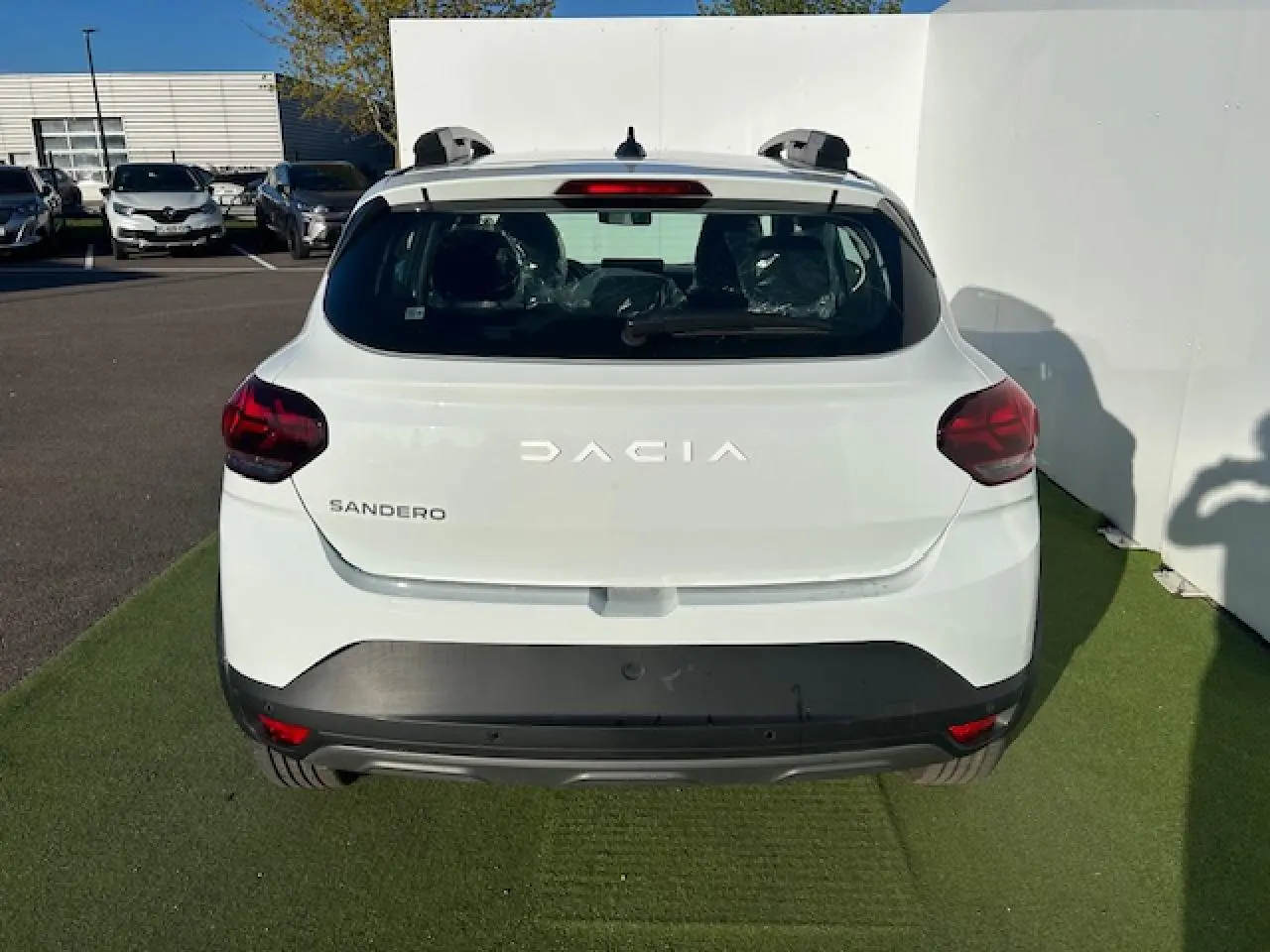 Vue arrière d'une Dacia Sandero blanche Arctic avec feux arrière en Y et barres de toit visibles.