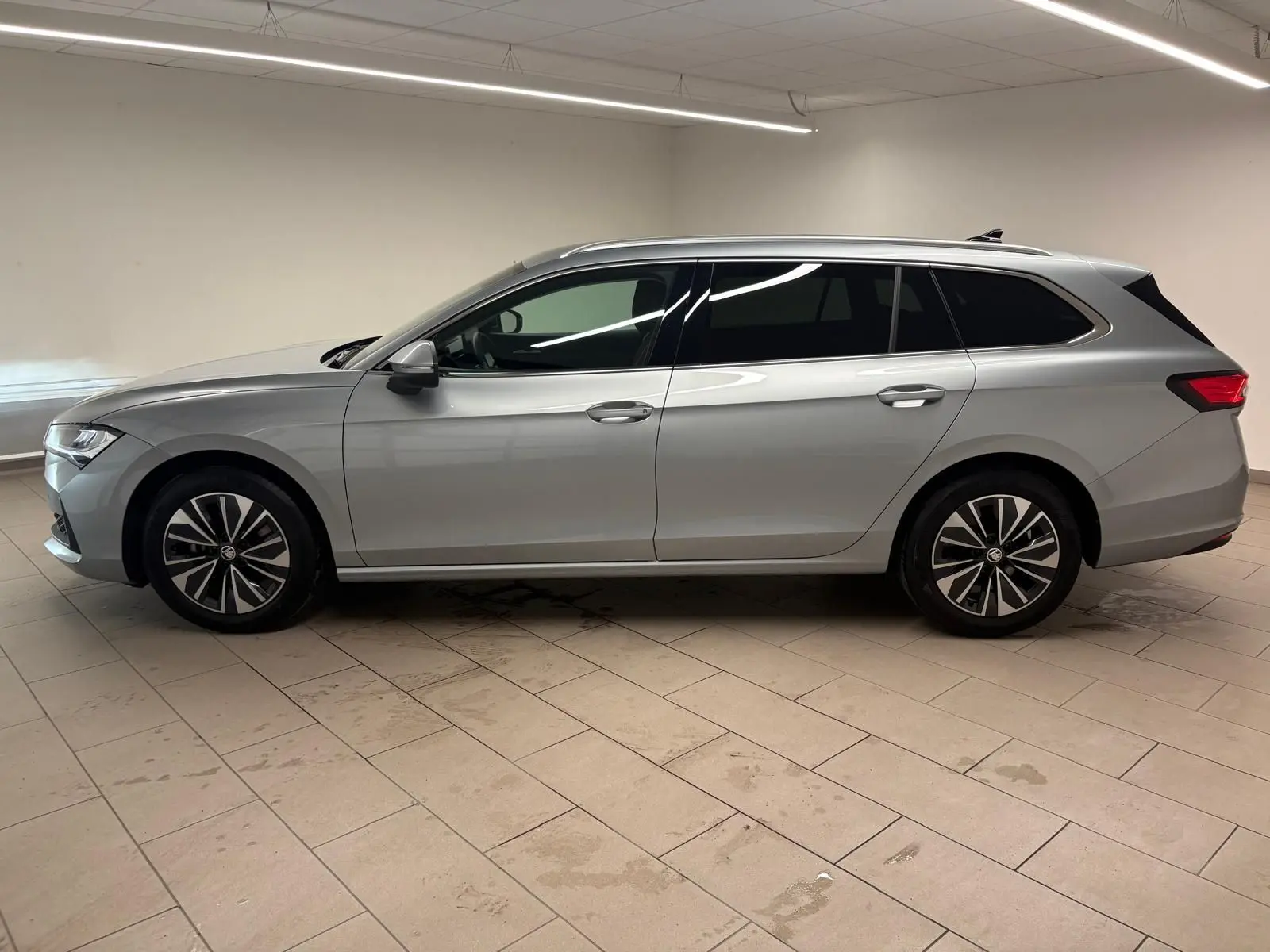 Vue de profil côté gauche d'une Skoda Superb Combi gris argent 2025 avec jantes alliage et vitres teintées.