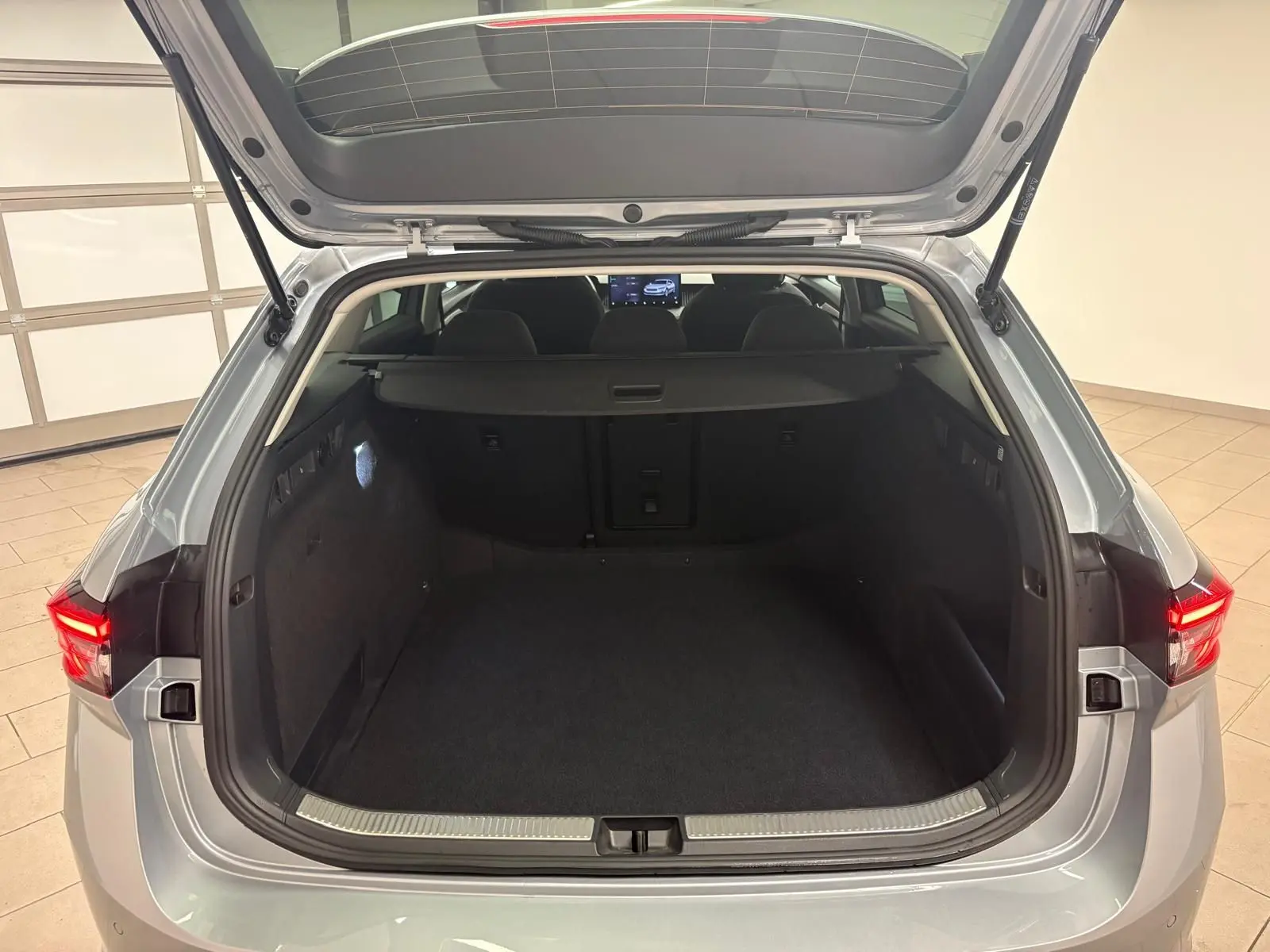 Coffre ouvert vu de l'arrière d'une Skoda Superb Combi gris argent 2025, intérieur spacieux et habillage noir.