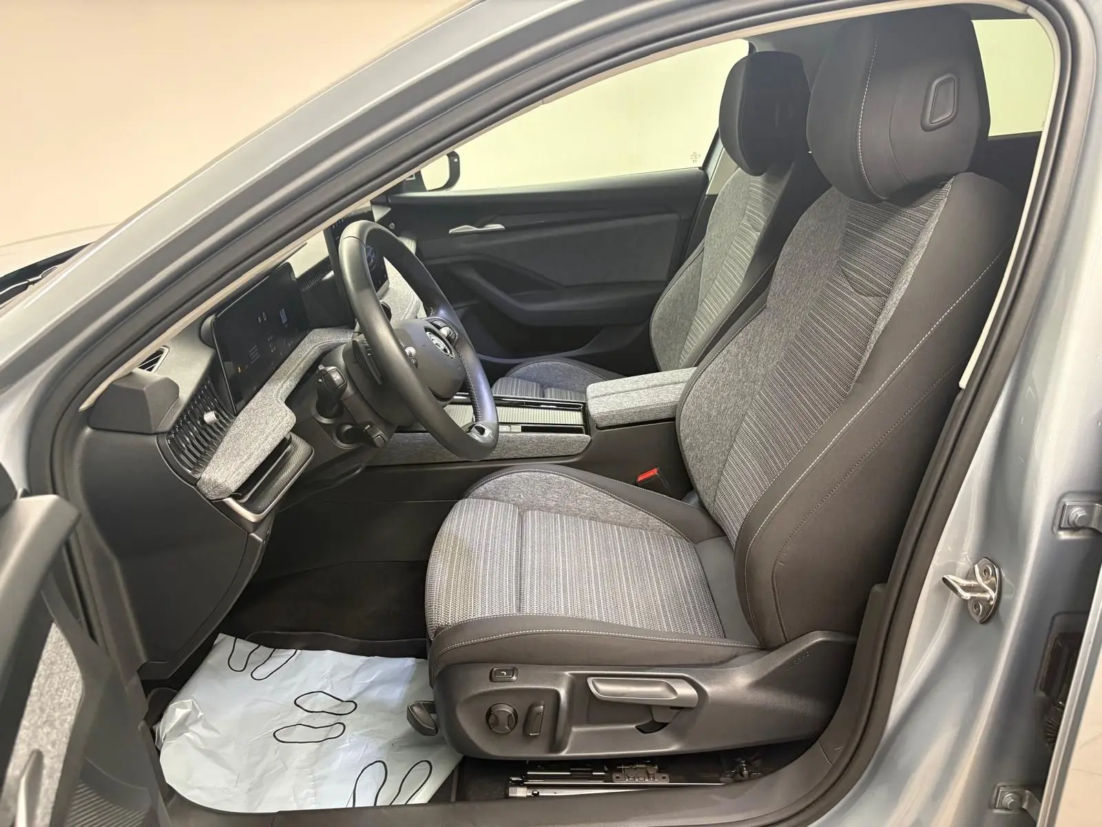 Vue intérieure côté conducteur de la Skoda Superb Combi 2025 gris argent, sièges tissu gris et tableau de bord moderne.
