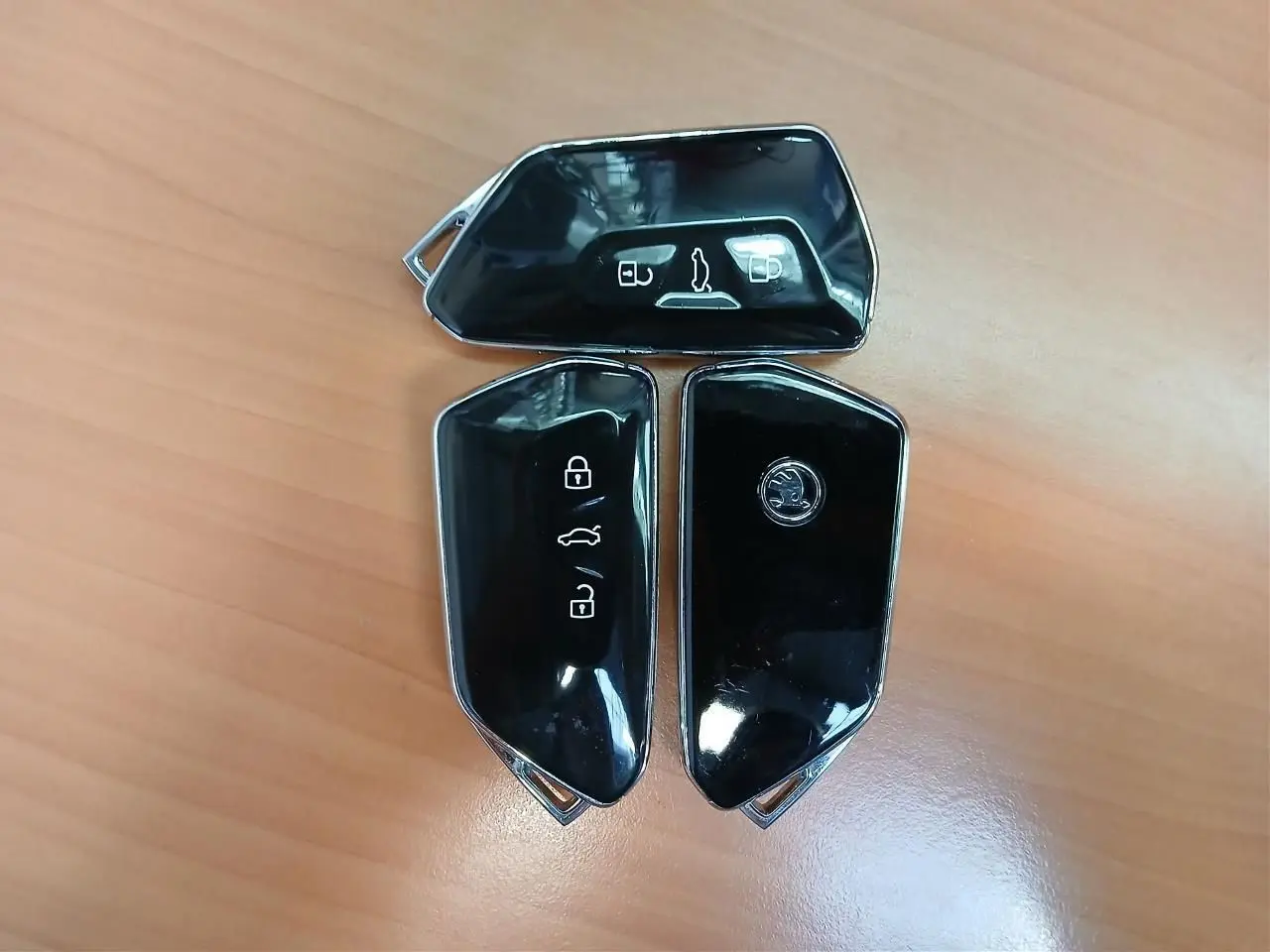 Trois clés noires brillantes de SKODA Superb Combi 2025 posées sur un bureau en bois clair.