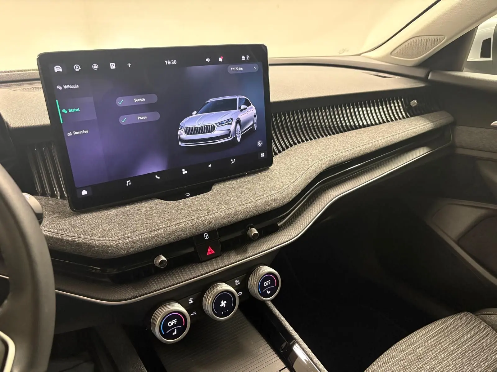 Vue intérieure côté passager du tableau de bord gris clair du Skoda Superb Combi 2025 avec écran tactile central et commandes climatisation.