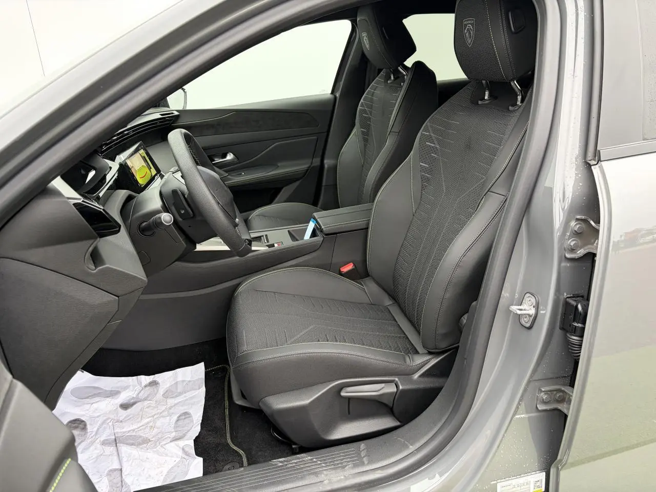 Vue intérieure côté conducteur de la Peugeot 308 gris selenium, sièges sport noirs avec surpiqûres vertes et tableau de bord moderne.