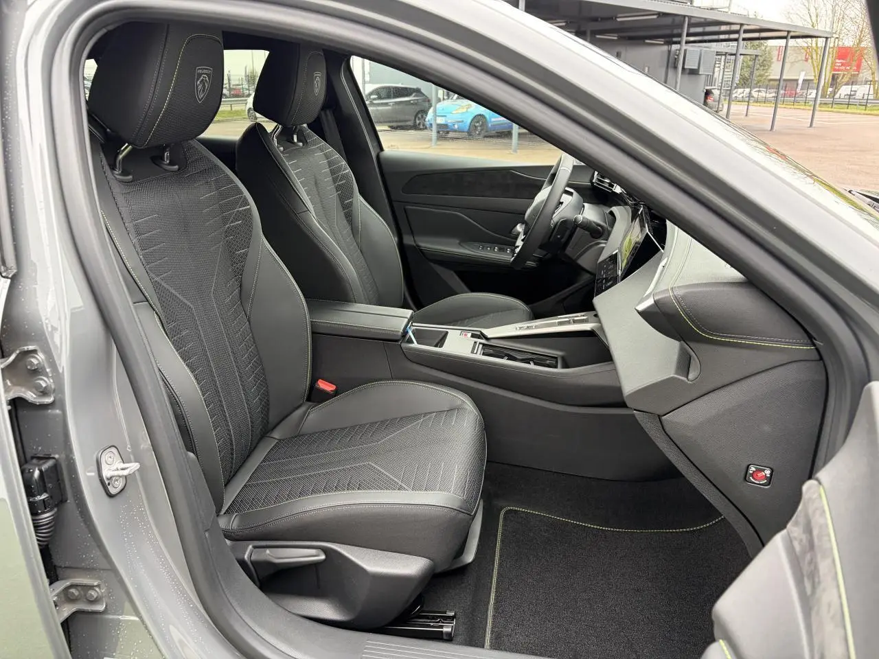Vue intérieure côté conducteur du Peugeot 308 gris selenium, sièges noirs avec surpiqûres vert Adamite et volant compact cuir.