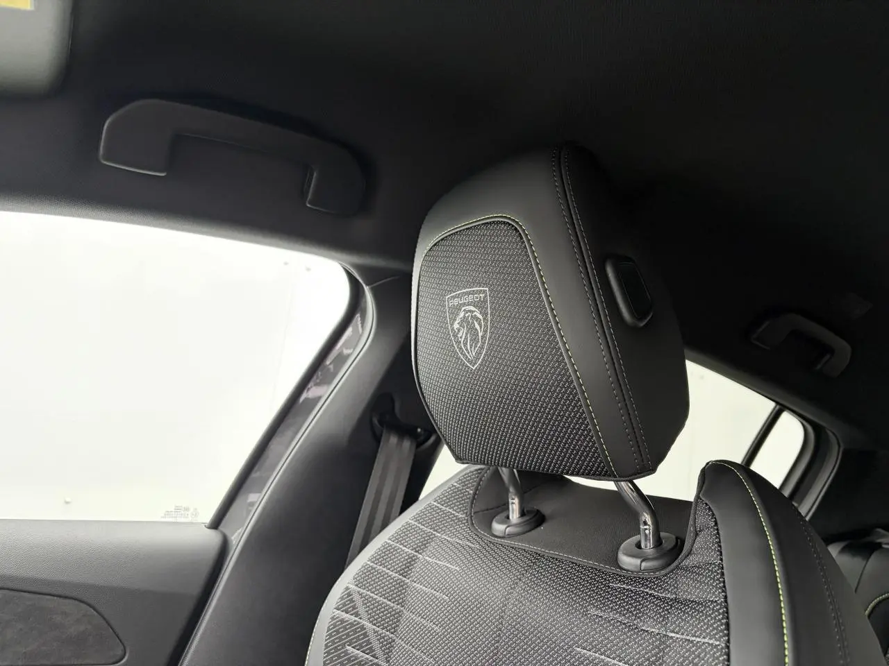 Gros plan sur l'appui-tête avant droit noir avec surpiqûres vert Adamite et logo Peugeot dans l'habitacle.